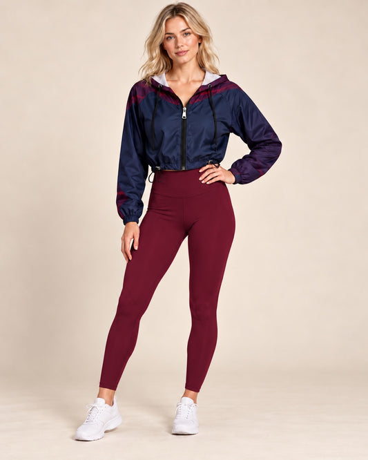 Blonde female model wearing DivineWear Dusk cropped windbreaker styled with wine-red leggings
