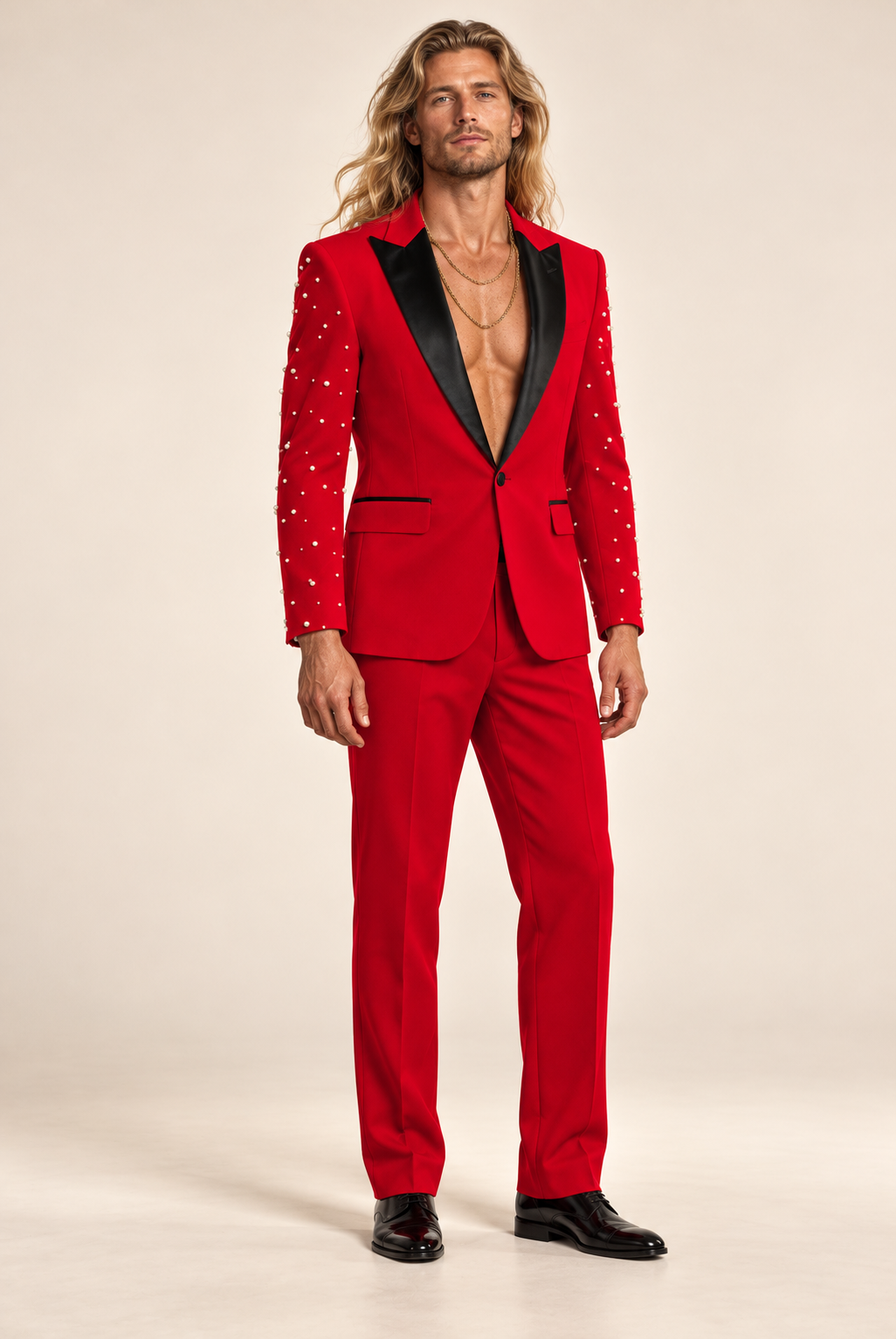 Long-haired blonde male model wearing DivineWear red faux pearl beaded runway suit with black satin lapels and two gold chains